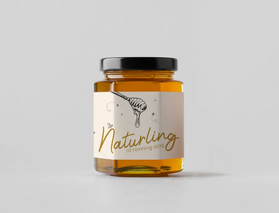 Medaus stiklainis su šviesia „Naturlig“ etikete, auksinės spalvos užrašu ir varvančio medaus šaukšto piešiniu.