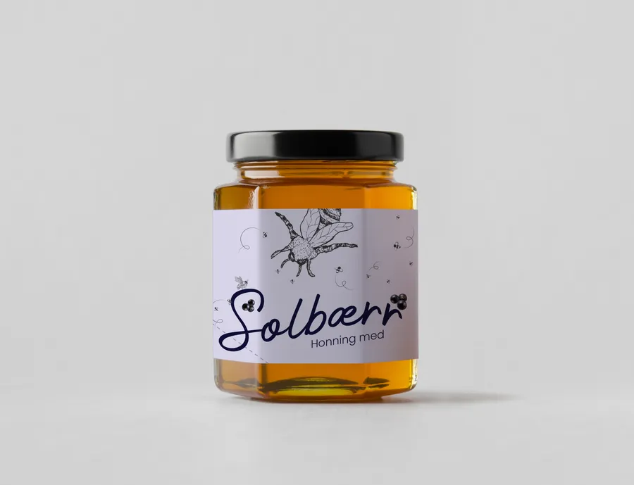 Medaus stiklainis su šviesiai violetine „Solbær“ etikete, tamsiu rankraštiniu pavadinimu ir uogų šakelės piešiniu.