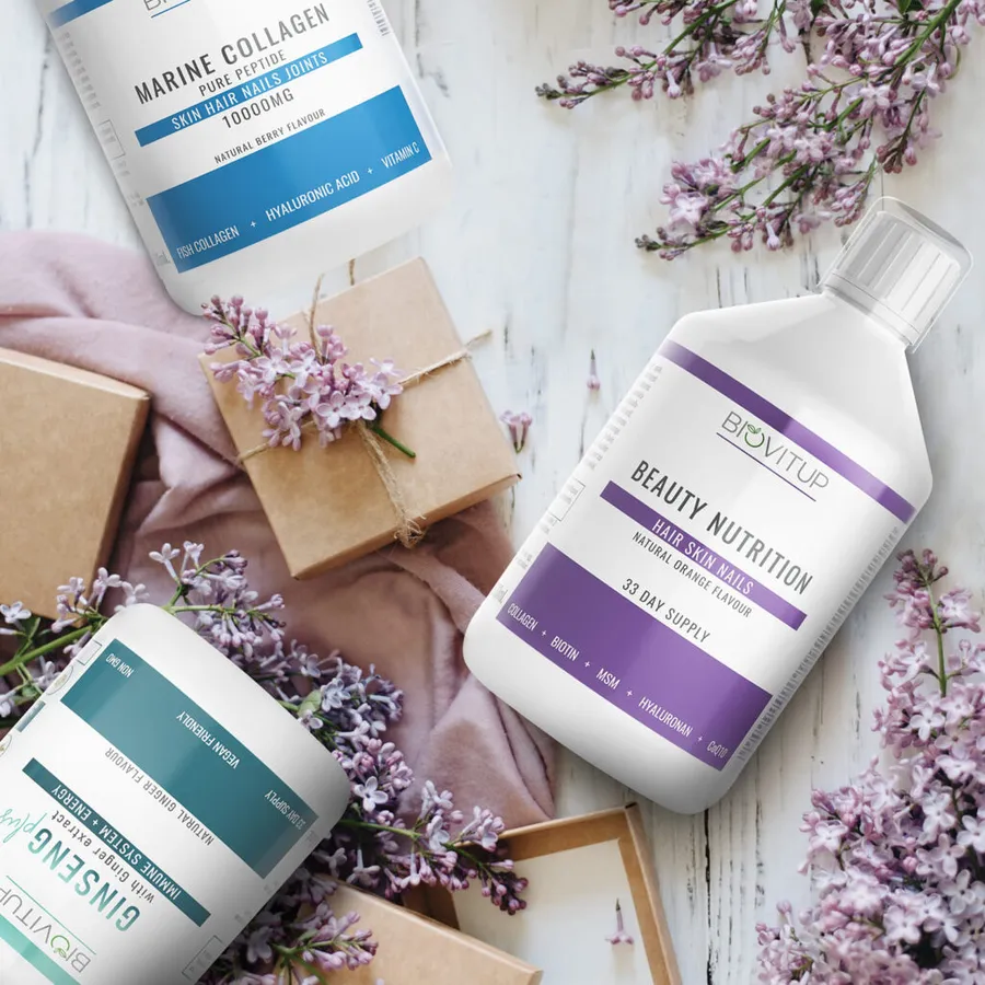 Biovitup papildų pakuotės su mėlynais, violetiniais ir žaliais etikečių akcentais tarp alyvų žiedų.